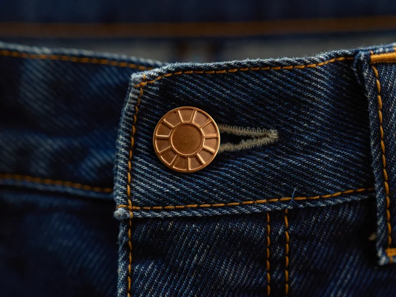 Illustration: Nahaufnahme von indigoblauem Denim mit Kontrastnaht und Kupfernieten