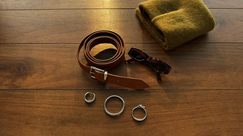 Illustration: Accessoires wie Gürtel, Schmuck, Schal und Sonnenbrille auf einem Holztisch
